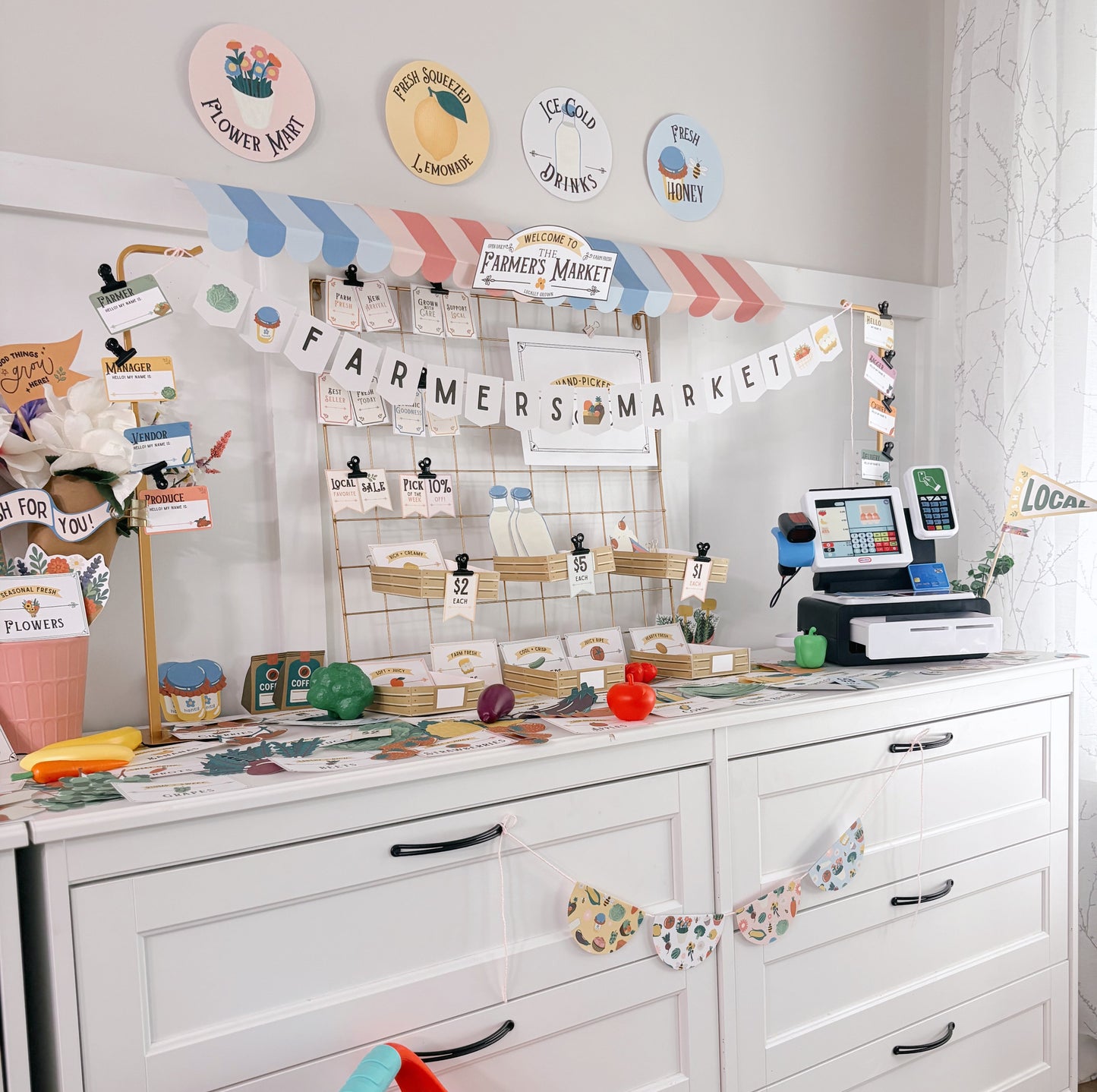 Children's play area with a white dresser, colorful toys, and a 'Farmers Market' themed wall display.
