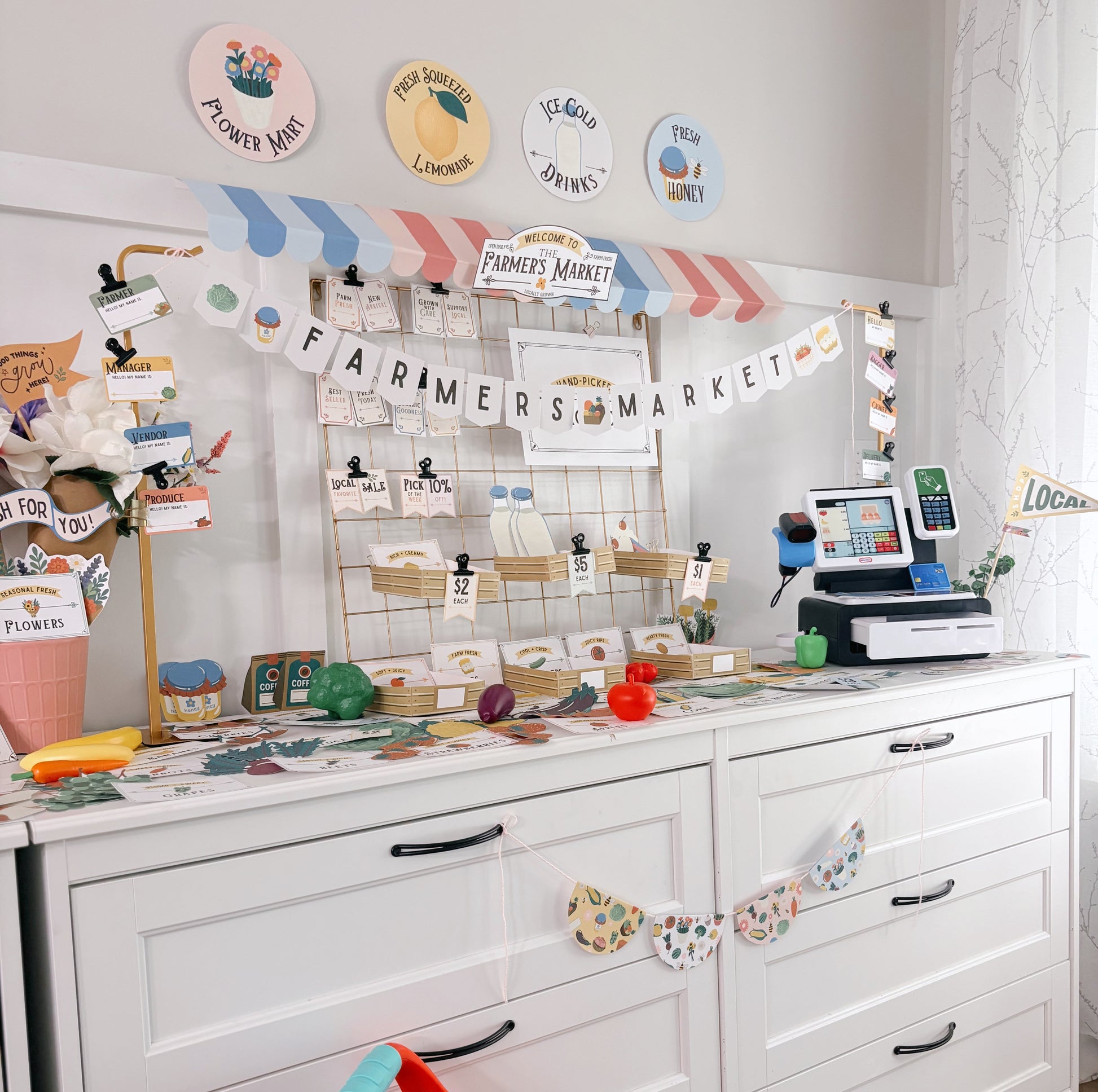Children's play area with a white dresser, colorful toys, and a 'Farmers Market' themed wall display.