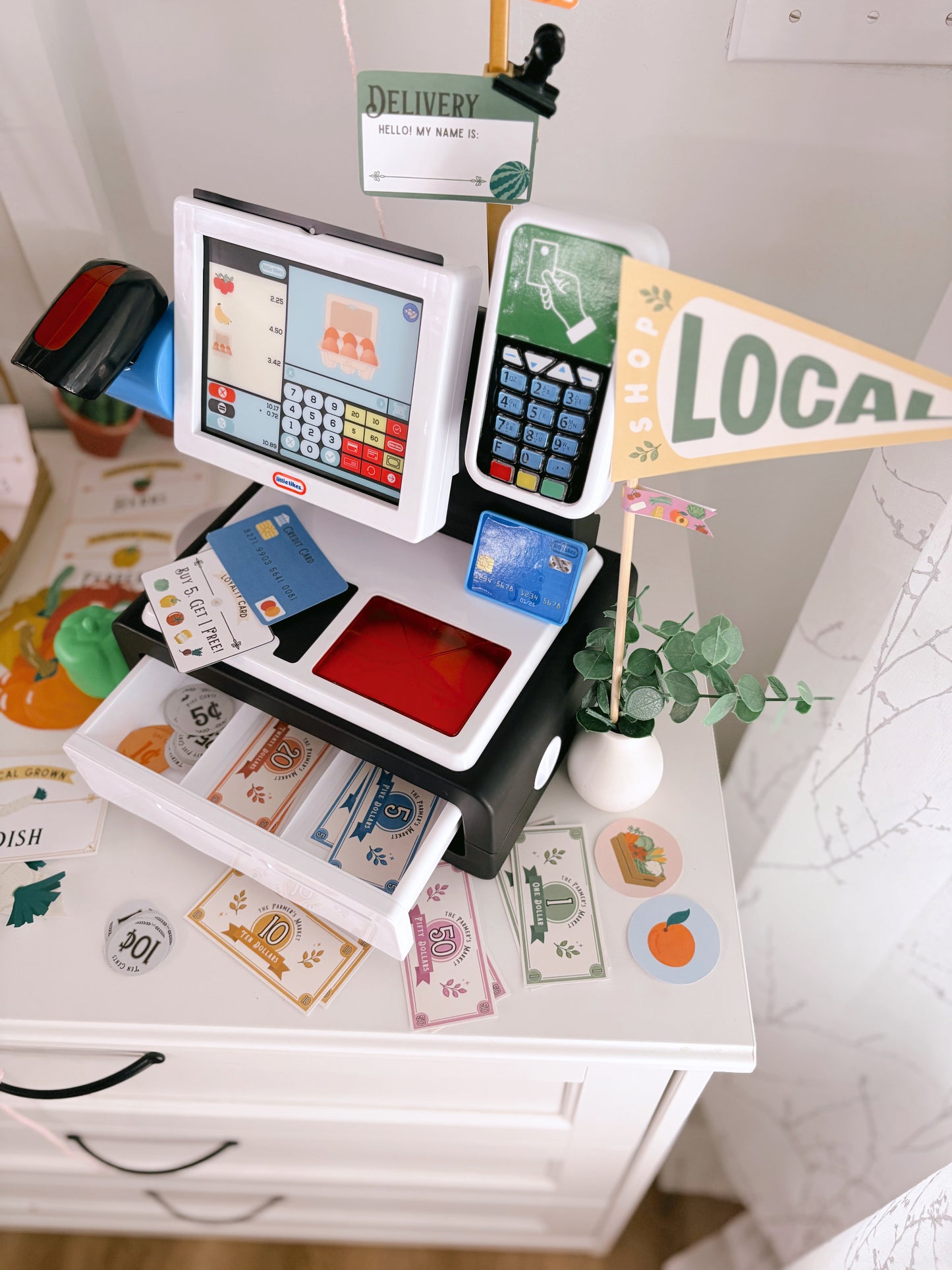 Miniature cash register with cards and a 'Local' sign on a white surface.