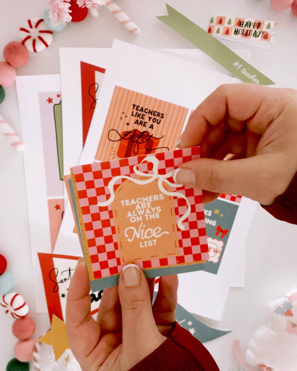 Hand holding a card with 'Teachers are always on the nice list' text, surrounded by other cards.