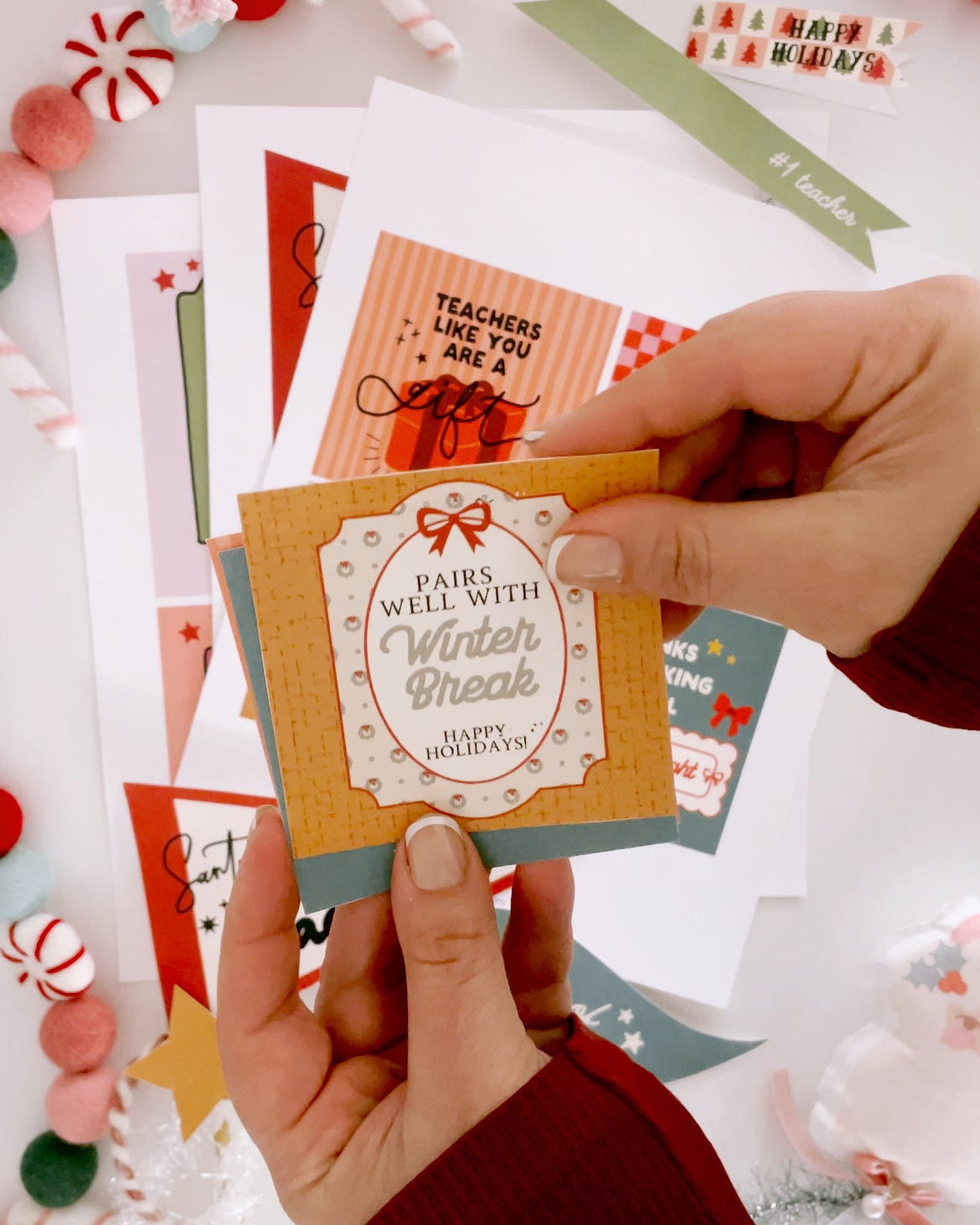 Hand holding a Christmas card with 'Pairs well with winter break' text, surrounded by other holiday cards.