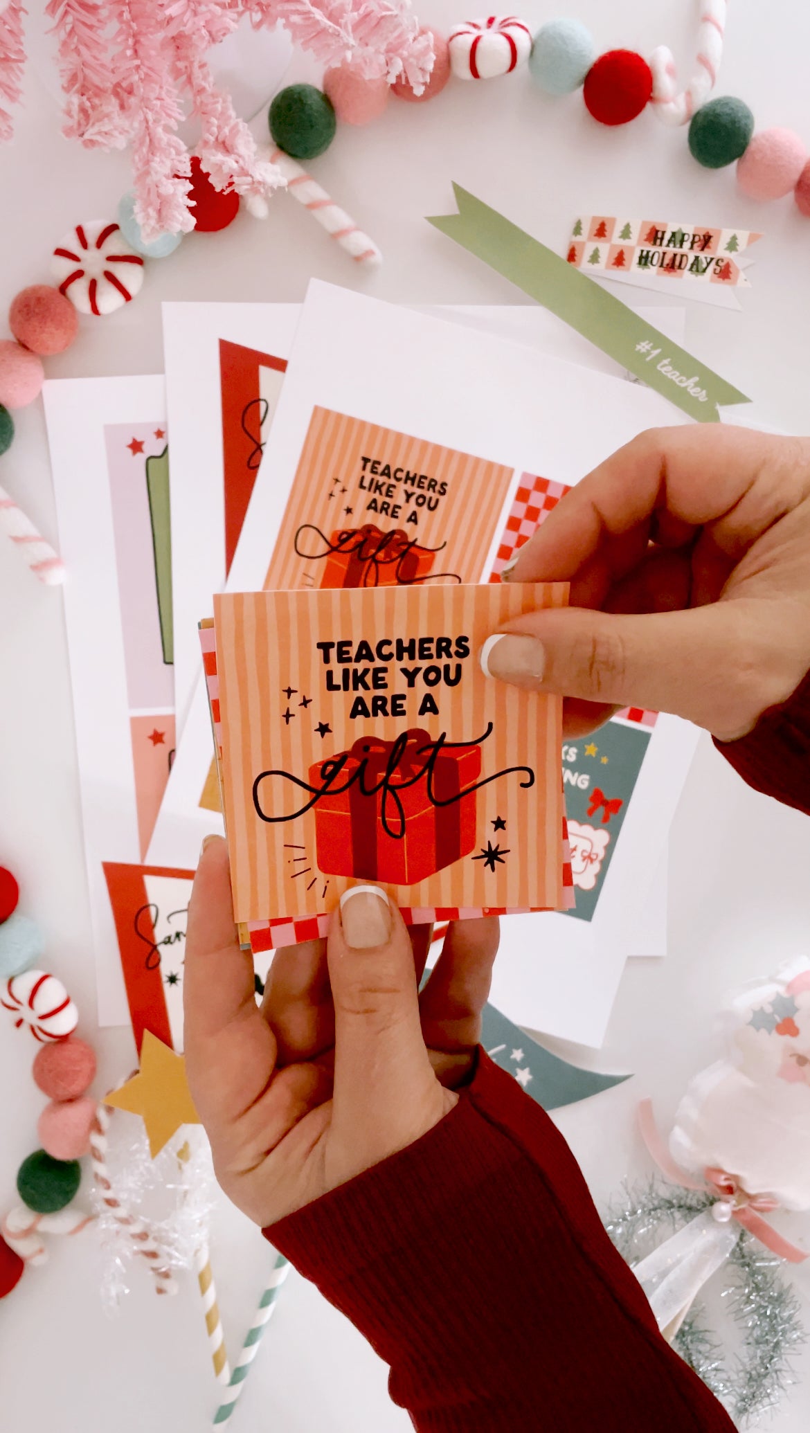 Hand holding a card with 'Teachers like you are a gift' text, surrounded by festive decorations.